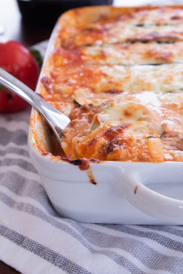 zucchini lasagna in a white casserole dish with a spoon coming out of it