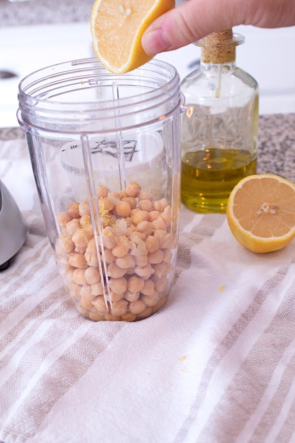 a nutribullet jar full of garbanzo beans with a lemon being squeezed