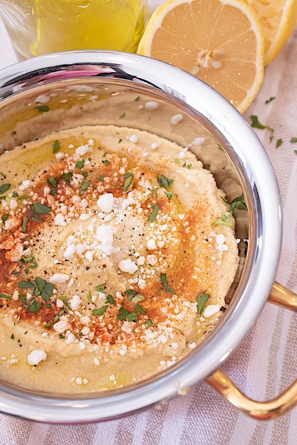 a copper dish full of no tahini hummus with feta olive oil and spices
