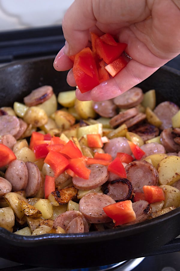 adding bell pepper to sausage and potato skillet