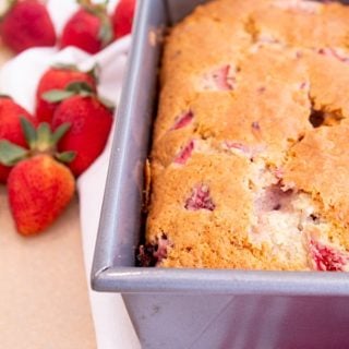 strawberry bread in loaf pan on red and white kitchen towel