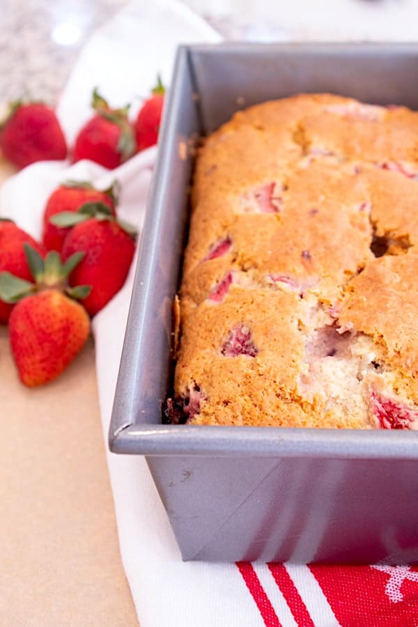 strawberry bread in loaf pan on red and white kitchen towel