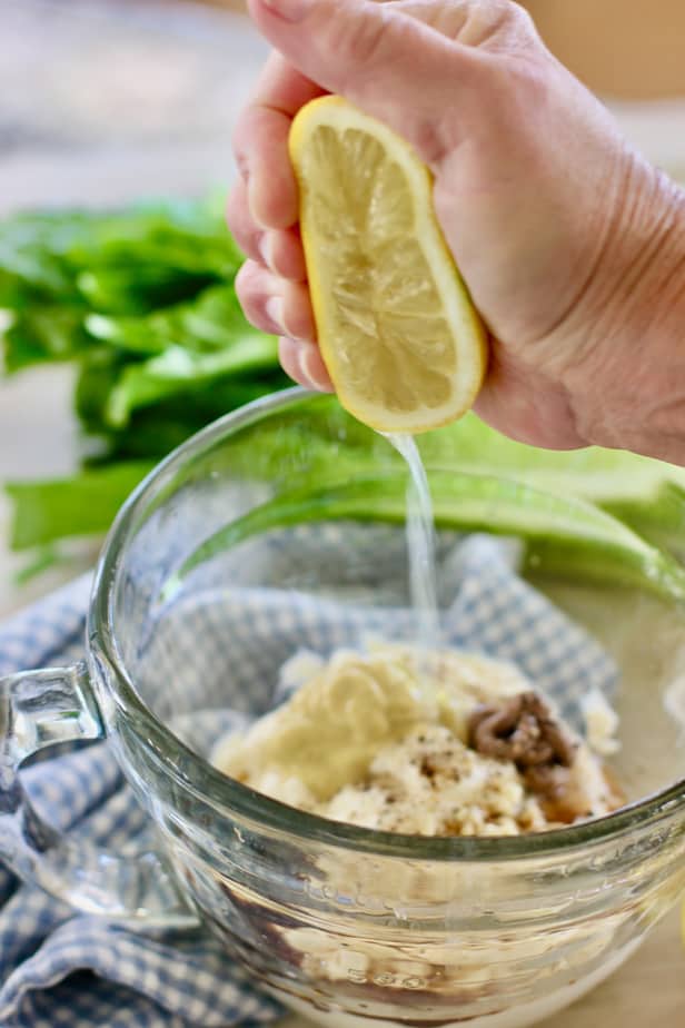 squeezing lemon into a clear bowl with caesar dressing ingredients