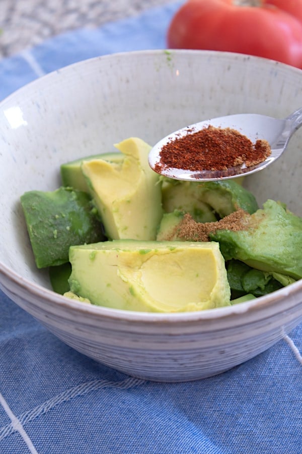 adding chili powder to bowl of avocado chunks