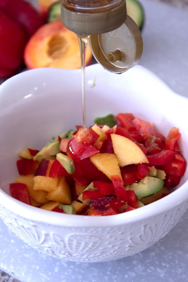 pouring honey on peach salsa into white bowl