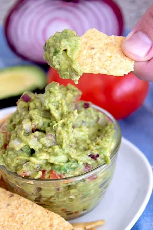 chip being dipped in guacamole in clear bowl