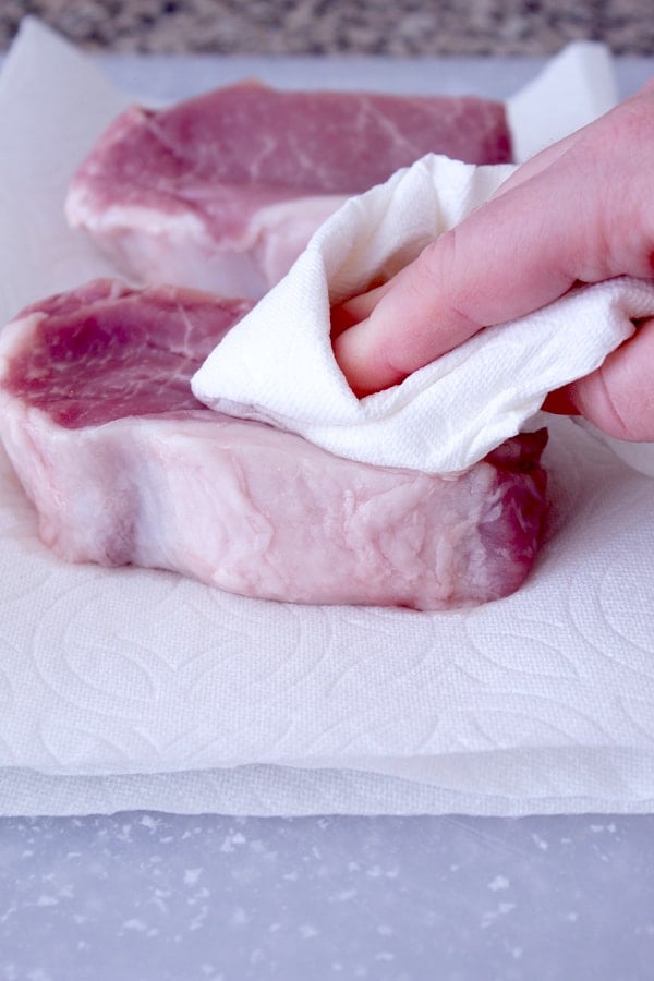 patting pork chop with a paper towel on a cutting board