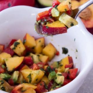 peach salsa in a white bowl on a spoon