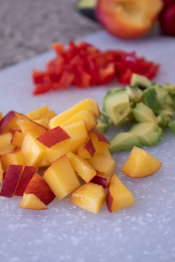 peach salsa ingredients chopped on a white cutting board