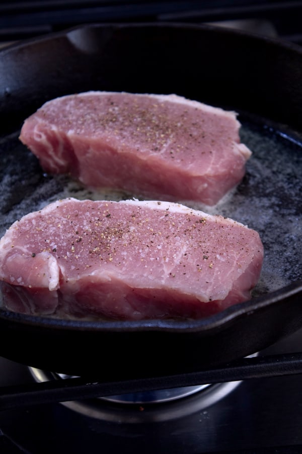 2 raw pork chops in a cast iron skillet 