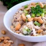 white bowl with asian rice salad in it garnished with parsley and whole cashews