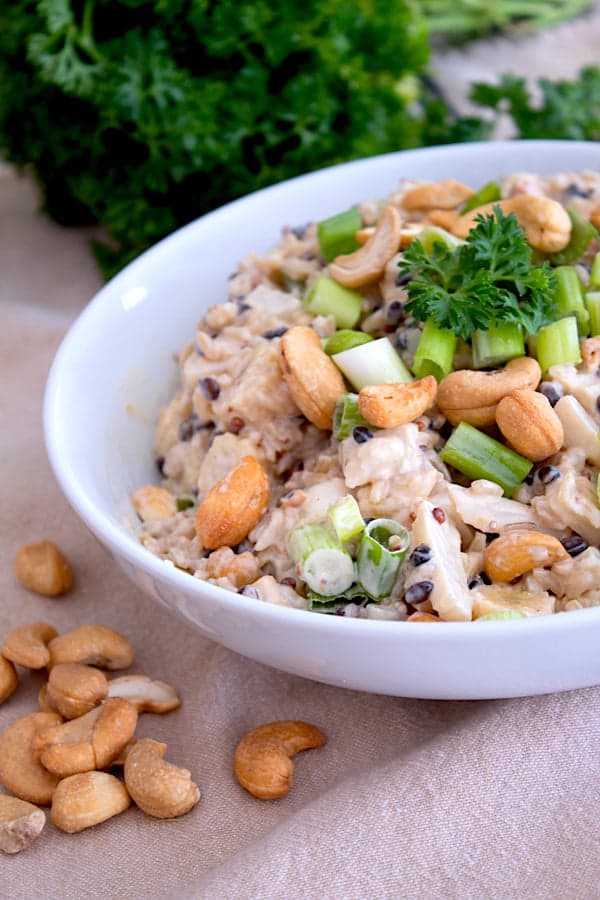 white bowl with asian rice salad in it garnished with parsley and whole cashews