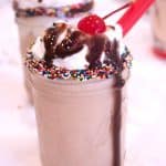 chocolate malt with chocolate syrup drizzle, nonpareil sprinkles and cherry on top with red straw in a mason jar