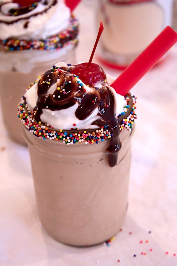 chocolate malt in a mason jar with sprinkle rim, chocolate sauce drizzle and cherry on top