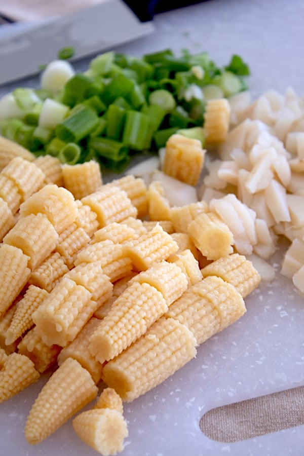 chopped baby corn, water chestnuts and spring onion on a cutting board