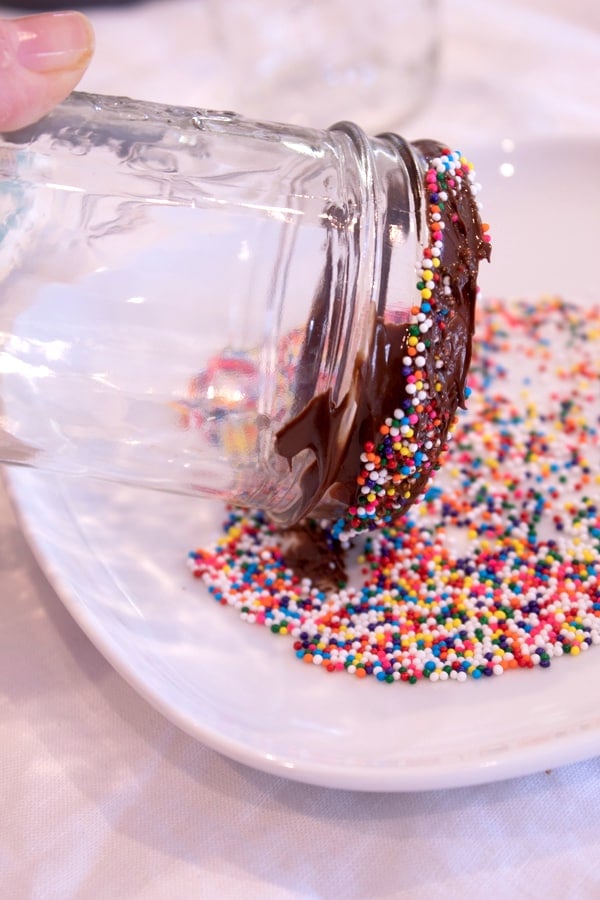 trempage d'un verre cerclé de chocolat dans une assiette de paillettes nonpareil de couleur