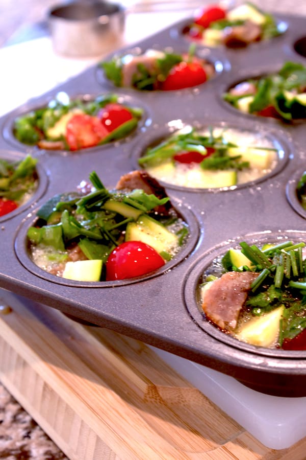a cupcake pan filled with frittata ingredients on a wooden cutting board