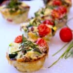 frittata muffins on a white cutting board with chives and red cherry tomatoes