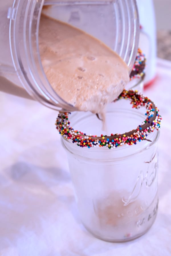 Milchshake in ein mit Schokolade und Streuseln verlinktes Kerr-Glas gießen