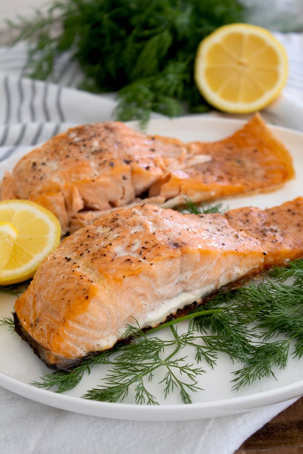 cooked salmon on a white plate with dill and lemon