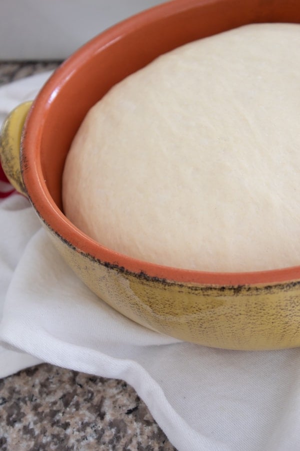 focaccia bread dough in a bowl after rising on a white towel 