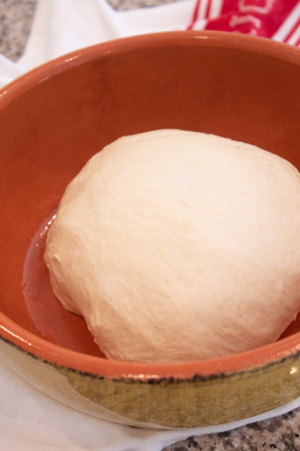 focaccia dough before rising in an orange terra cotta bowl