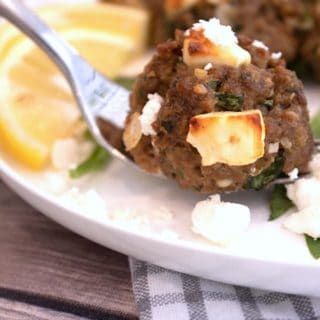 greek meatballs on a fork on a white plate with lemon and crumbly feta cheese