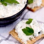 Boursin style cheese on a triscut cracker with fresh parsley on a white tea towel