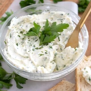 overhead view of Boursin cheese in a clear bowl surrounded by bread and herbs
