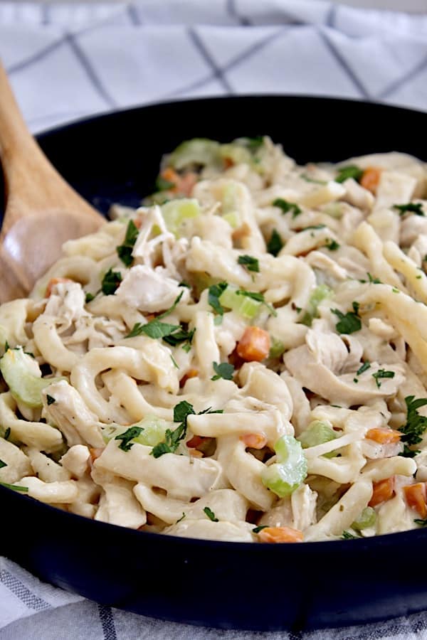 a black skillet with homemade chicken and noodles garnished with parsley flakes