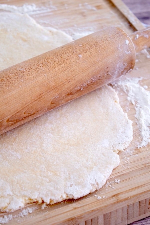 rolling out egg noodle dough with rolling pin on cutting board