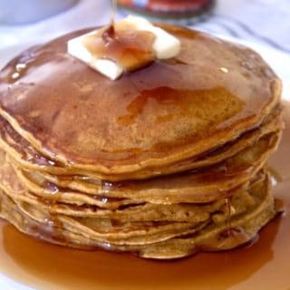 stack of pumpkin pancakes with butter and syrup on a white plate