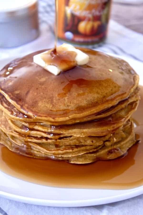 stack of pumpkin pancakes with butter and syrup on a white plate