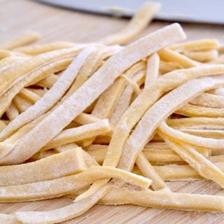 pile of raw egg noodles on cutting board with knife in background