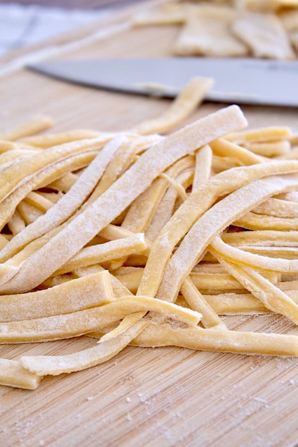 pile of raw egg noodles on cutting board with knife in background