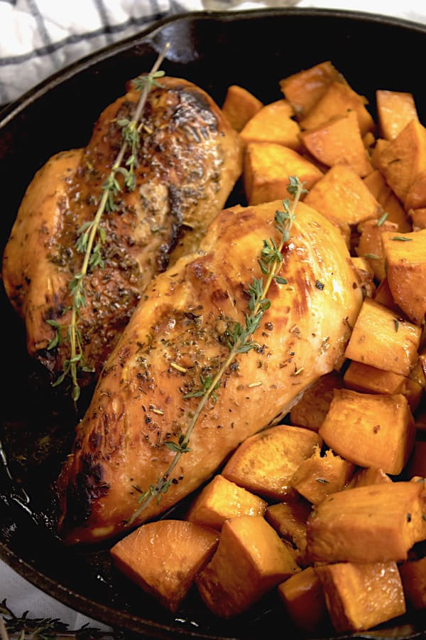 honey glazed chicken and sweet potatoes garnished with thyme in a cast iron skillet