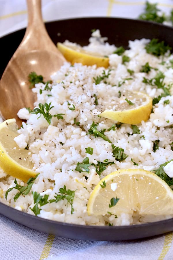 skillet of rice with lemon wedges and parsley in a black skillet