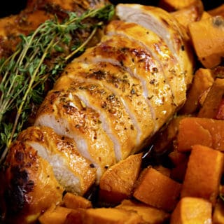sliced honey glazed chicken with sweet potatoes garnished with thyme in a cast iron pan