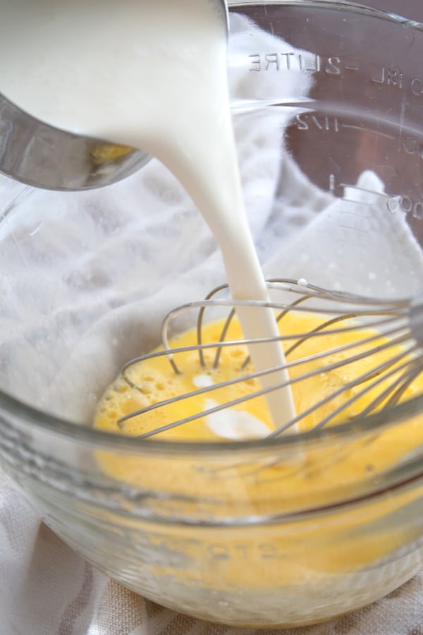 adding cream to egg mixture in a clear mixing bowl