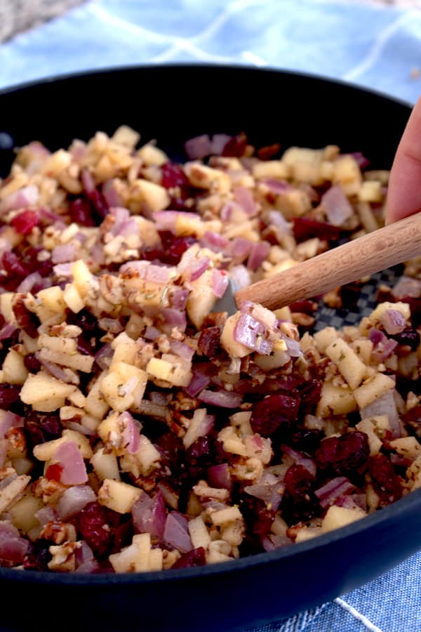 sautéing apples cranberries onions and pecans in a black pan