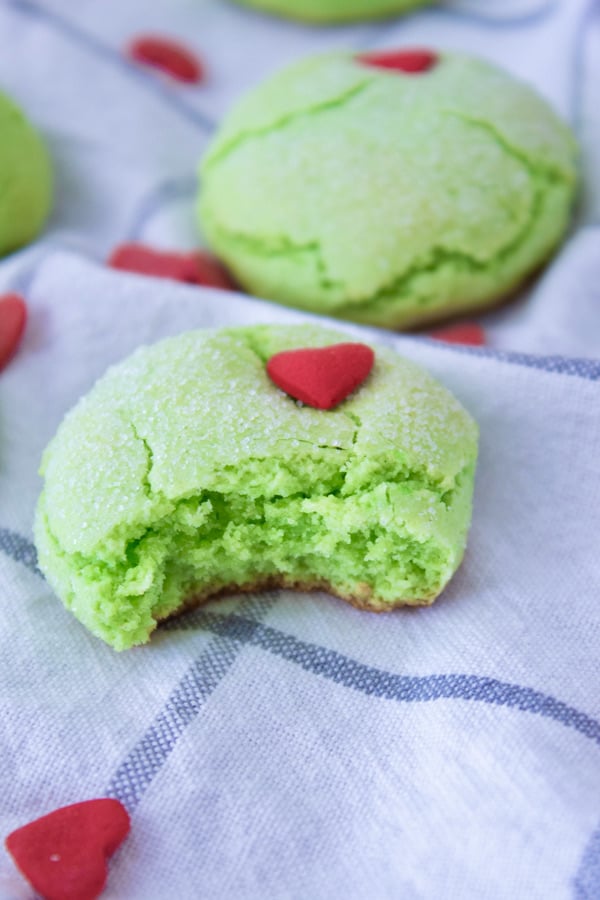 a green cookie with a bite out of it with red heart sprinkle