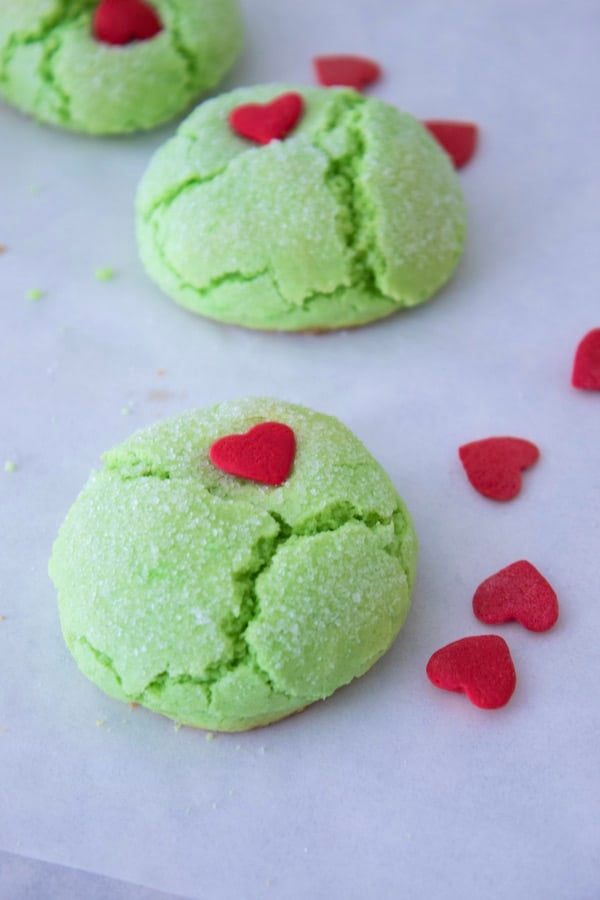 3 grinch green cookies on white parchment with red heart sprinkles