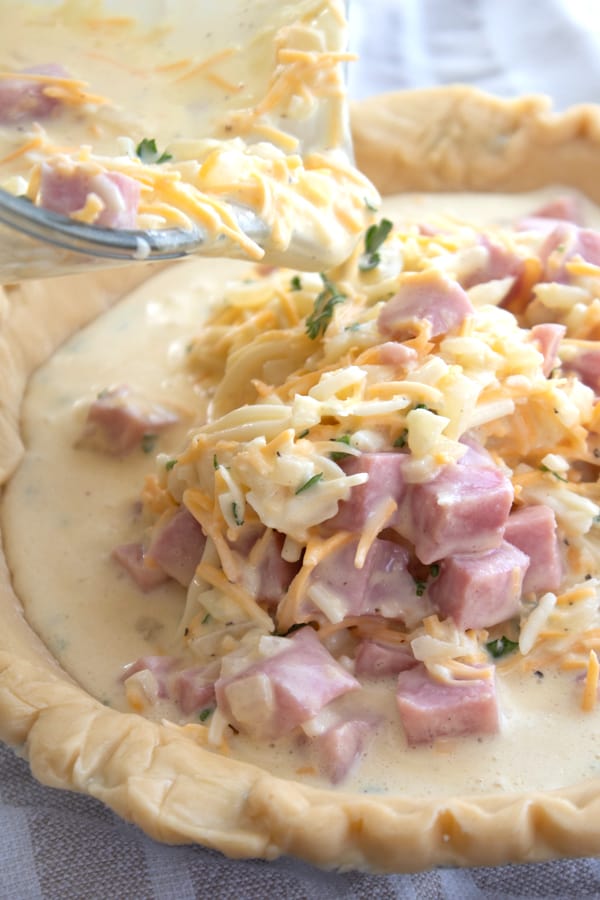 pouring quiche mixture in a pie crust