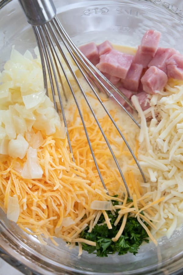 showing top of mixing bowl with onions, ham, cheese parsley and egg mixture