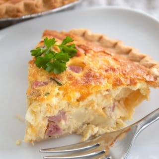 a slice of quiche on a white plate with a fork and parsley garnish
