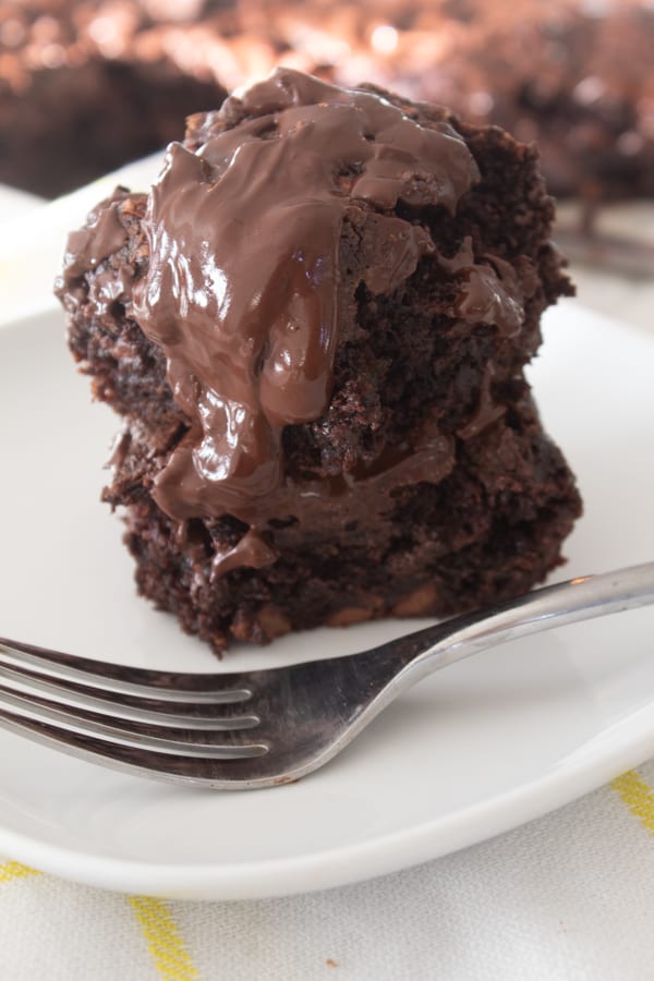 2 zucchini brownies stacked on a plate with a fork and chocolate dripping down