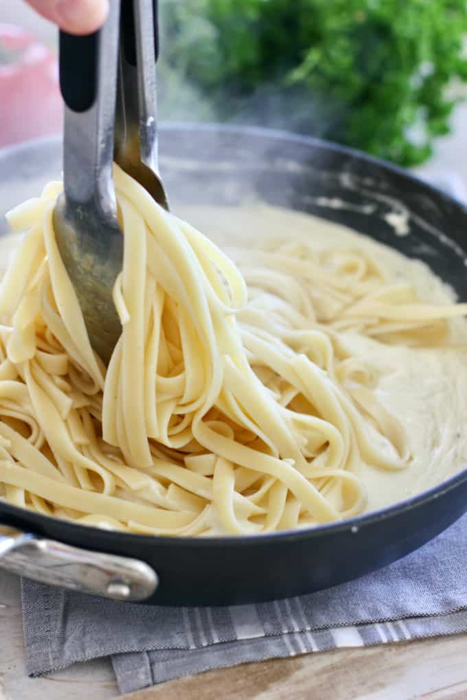 hot pasta being tossed into fettucine alfredo sauce