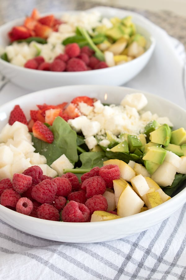 adding ingredients to salad in white bowl