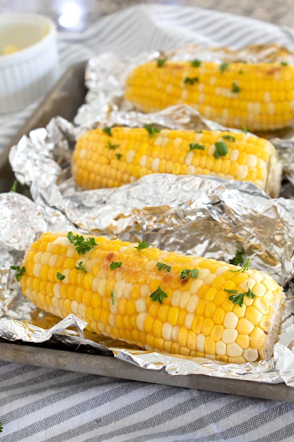 corn on the Cobb on foil on a sheet pan garnished with parsley