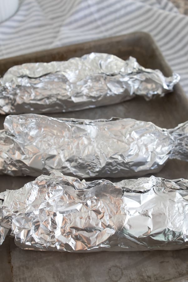 wrapped ears of corn in foil on a sheet pan